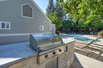A stainless steel grill is on a patio next to a pool.